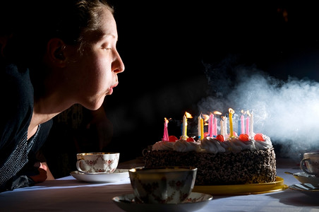 正在燃烧的蜡烛摄影照片_一个年轻的女人正在吹蛋糕上的蜡烛