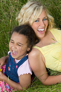 花与少女摄影照片_一位美丽的金发碧眼的年轻女子在一片长草的田野上与一个混血少女玩耍