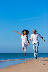 一对夫妇--黑人女性和高加索男性--在假期中沿着海滩散步和跑步