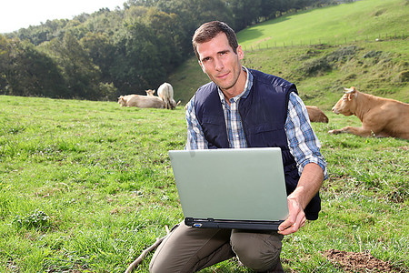 饲养员摄影照片_饲养员拿着笔记本电脑坐在牛场里