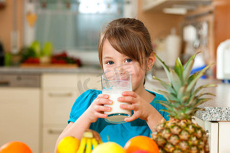 健康饮食-儿童饮用牛奶，前面的桌子上放着大量新鲜水果