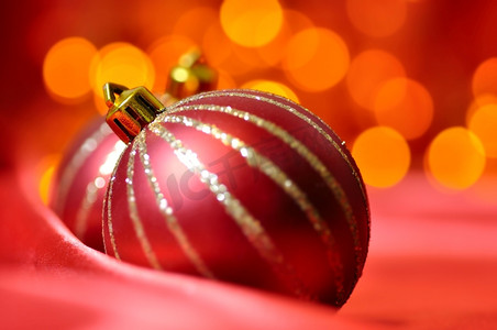 圣诞装饰球摄影照片_红色丝绸上的圣诞装饰球在背景模糊灯光的映衬下