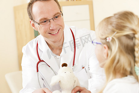医生--儿科医生--和他诊所里的一位儿童病人在一起，她正用她的柔软玩具来感谢他。