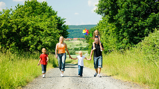 阳光明媚的夏日，幸福的一家人走在一条小路上