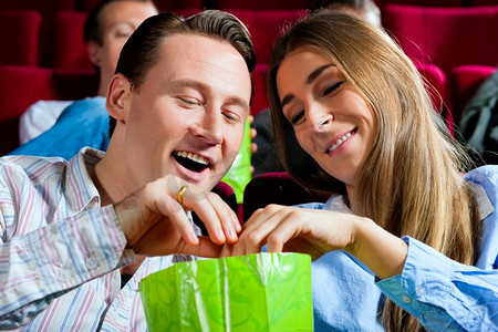 电影观影摄影照片_一对情侣在电影院看电影；他们吃爆米花