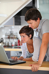 年轻夫妇拿着笔记本电脑站在厨房里