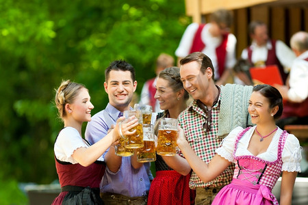 酒吧乐队摄影照片_在啤酒花园在巴伐利亚州，德国-朋友在Tracht，Dirndl和Lederhosen和Dirndl站在前面的乐队