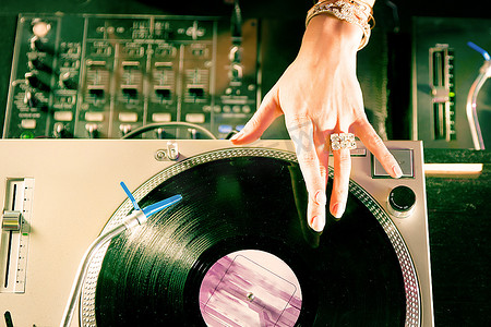俱乐部转盘上的女DJ，和调音台和老式唱片机在一起