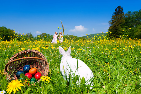 彩蛋蓝色摄影照片_春天，草地上的复活节兔子带着彩蛋，背景是两个孩子