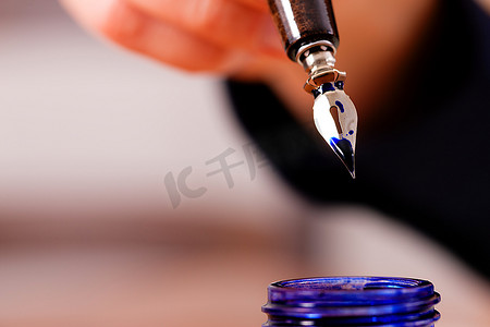 用钢笔和墨水在纸上写字的人(只有一只手)，前景中有一个墨水罐
