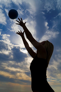 一名年轻女子在海滩上练球，在戏剧性的清晨天空的映衬下，她的剪影清晰可见