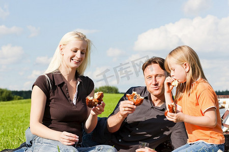 一家人--父亲、母亲和女儿孩子--在一个美丽明媚的夏日，在绿色的草地上野餐