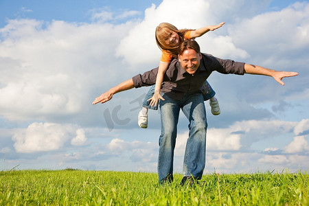 父亲和他的儿女一起在草地上玩耍，他背着她