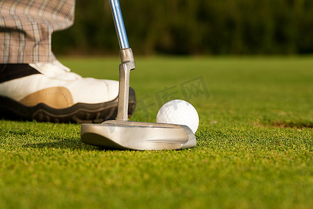 高尔夫球手试图将球打进球洞，近距离击打高尔夫球杆、球洞和人的脚