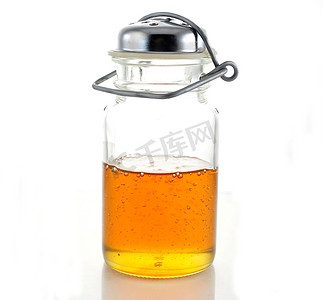 粘稠的液体摄影照片_白色背景的玻璃瓶里的蜂蜜