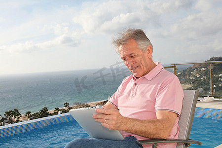 一位老人在游泳池边使用电子平板电脑