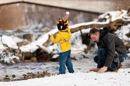 雪球摄影照片_一家人--父亲和儿子--冬天沿着河岸散步；孩子在扔雪球