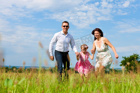 幸福的家庭--母亲、父亲、孩子--夏天在绿色的草地上奔跑