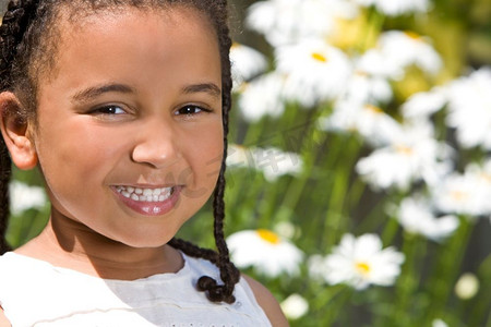 在灿烂的阳光下摄影照片_一个美丽的混血小女孩微笑着，在夏日灿烂的阳光下，背靠着巨大的雏菊