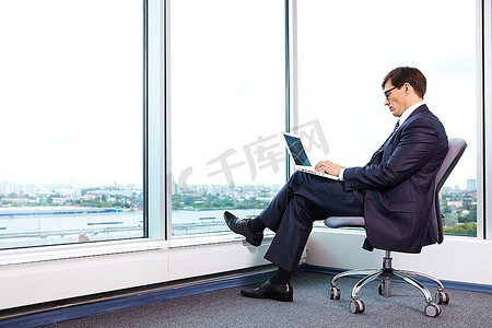 主任在办公室里用笔记本电脑在一扇大窗户的背景下工作
