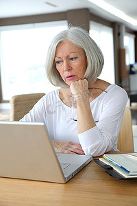 高级妇女在家在膝上型计算机前面