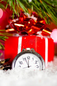 圣诞树树枝摄影照片_雪地上的礼盒和时钟，背景模糊的圣诞树树枝