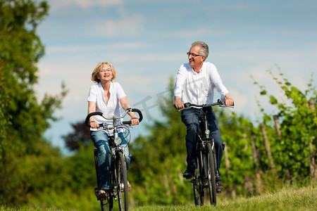 已经预约摄影照片_幸福的成熟夫妇-老年人，男人和女人，已经退休-在大自然的夏天骑自行车