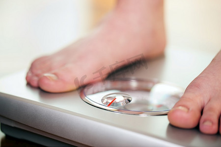 女人(只能看到她的脚)站在浴室秤上测量体重，控制她的节食结果