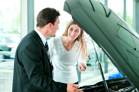 一名女子在经销商处买车，仔细查看发动机。