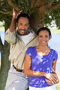一对幸福的非裔美国夫妇站在外面的一棵树下，手牵着手。