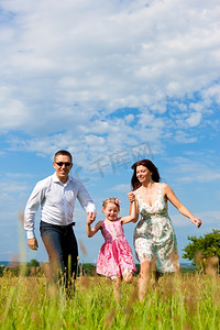幸福的家庭--母亲、父亲、孩子--夏天在绿色的草地上奔跑