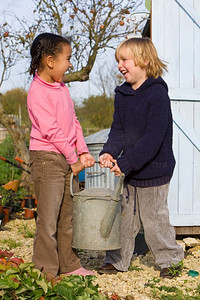 喷壶摄影照片_秋天的花园里，两个小孩提着一个沉重的喷壶