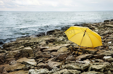 概念，冰冷的大海和灰色的石头聚焦在黄色的伞上