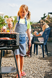 举办烧烤派对的家庭--小孩子在烧烤架上准备肉类和香肠