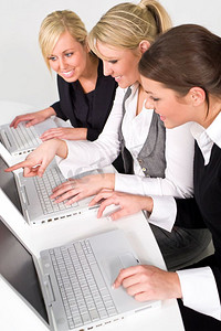 一个由三名年轻女商人组成的团队在她们的笔记本电脑上工作，这张照片的焦点是中间的女人