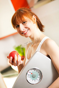 苗条美丽的女人(只有躯干)用卷尺测量自己的腰围，背景是碗里的水果