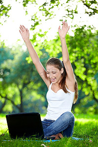 一个微笑的女孩与他的手了一台笔记本电脑在公园里