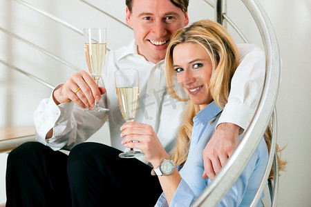 商务夫妇--男女--在家中，坐在公寓的楼梯上喝着香槟