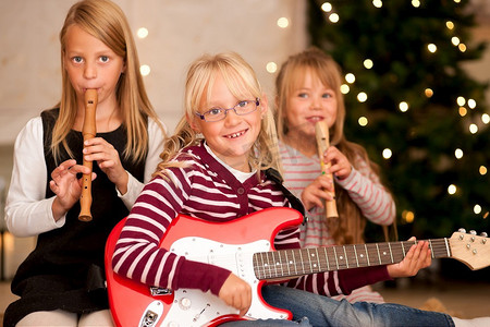 小孩子们拿着吉他和笛子--大概是礼物--在圣诞树前演奏音乐