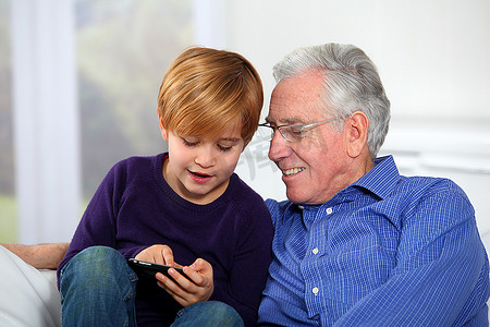 带孩子的老人摄影照片_老人带着小男孩在电话里玩电子游戏