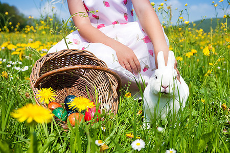 小女孩抚摸复活节兔子在草地上在春天