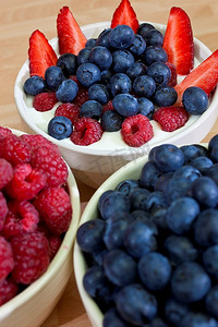吃蓝莓摄影照片_一碗健康早餐草莓、覆盆子和蓝莓在纯酸奶中，前景是一碗覆盆子和蓝莓