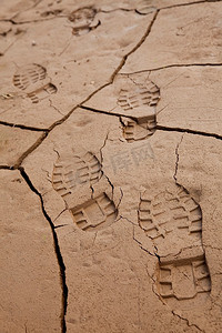 环境概念照片，展示了在干涸的湖床或河床上穿过干裂的泥土时留下的靴印。