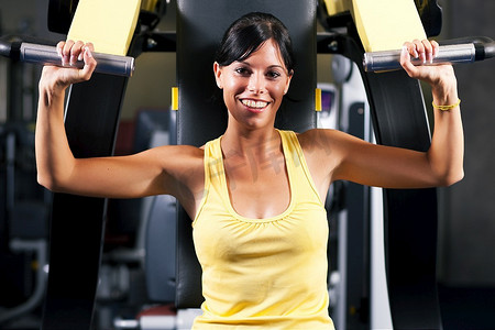 健身器摄影照片_健身房里非常健康和美丽的年轻女子在健身器上锻炼和举重