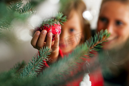 小女孩帮妈妈装饰圣诞树，手里拿着一些圣诞小玩意儿(重点放在小玩意儿上)