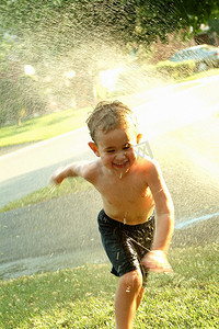 小男孩跑过夏天的洒水车。