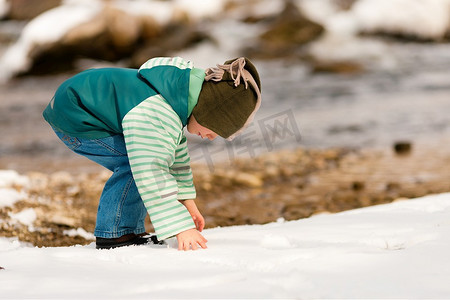 冬天在河边散步的小男孩；这个孩子正在堆雪球