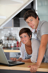 年轻夫妇拿着笔记本电脑站在厨房里