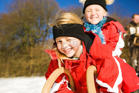 两个小孩子在雪地里的山顶上拉着雪橇，等着开始玩