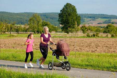 家庭运动--在阳光明媚的日子里，母女俩推着婴儿推车沿着小路慢跑